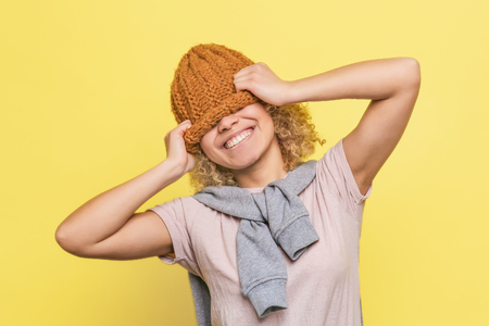 Funny and attractive girl has stretched the hat. She has put it on her eyes and smiling. Girl looks happy. Isolated on yellow backgroundの写真素材