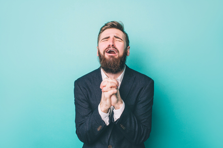 Guy is standing and holding his hands together. He is praying and begging. Also he is yelling. Isolated on blue background