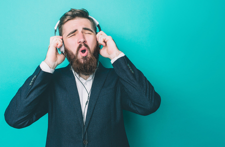 Amazing man is listening to the music through big headphones. He is singing and enjoying the moment. Isolated on blue backgroundの写真素材