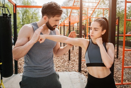 Handsome and strong man is training his student. He is teaching her. Girl is holding her hand straight and keeping her fingers in a fist.の写真素材