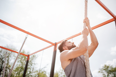 Another picture of a man climbing up. He uses rope for that. He is looking up. He exercises outside.の写真素材