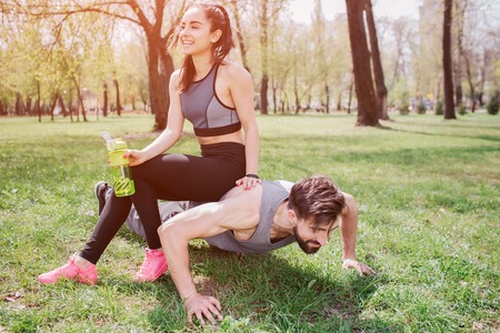 Funny picture of young man and woman. He is doing push ups and looking straight while she is sitting...