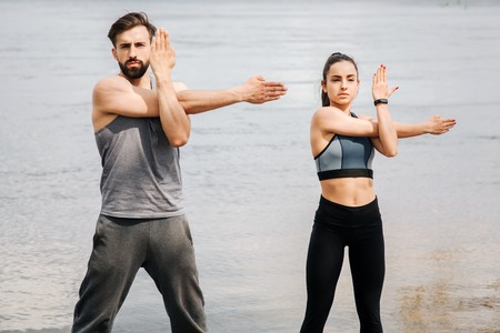 Two people are standing at the wall and working out. They has crossed their hands. This couple is warming up and stretching. They look serious and concentrated.の写真素材