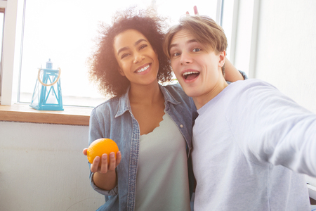 Two happy students are taking selfie. Girl is holding an orange ana smiling while the guy is holding a camera and laking pictures.の写真素材