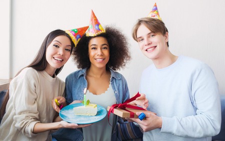 Nice picture of a birthday girl and her friends. Asian girl has a piece of cake. The guy holds a present in his hands. All of them are happy.の写真素材