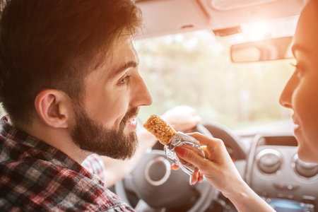 Cut view of a handsome man looking at his girlfriend and smiling. She is looking at him as well. She is going to feed guy with a sweet bar.の写真素材