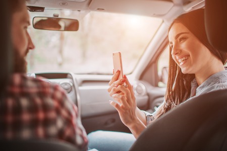 Young woman is taking picture of her man. She is looking at phone and smiling. She is doing that in...