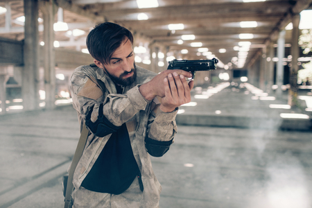 A picture of handsome and professional soldier taking aim. He is doing that by looking straight...