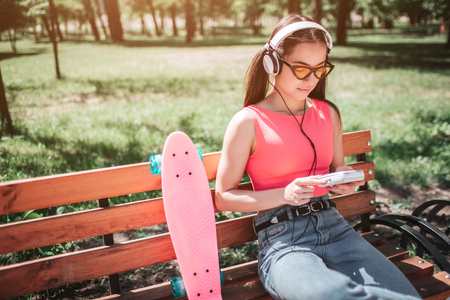 Calm and peaceful girl is sitting on bench outside and looking at her music player.の写真素材