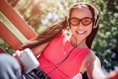 Positive and happy girl in weird glasses is taking selfie. She is smiling to camera. Girl is listening to music through headphones.の写真素材