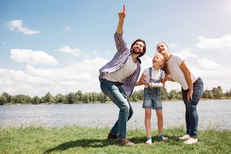 Nice picture of young family looking up in the sky. Guy is pointing up. Girl has a control panel on hands. Parents are holding their daughter back. They are happy.の写真素材