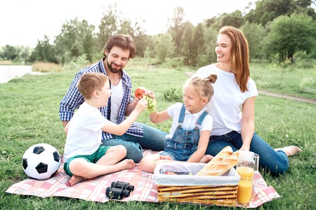People from one family is sitting together and having fun. Kids are splitting grapes whiile man has an apple in hand. Woman is looking at it and laughing.の写真素材