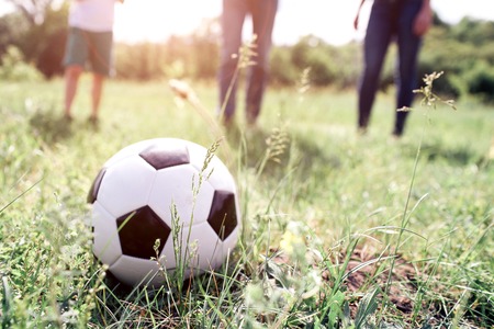 A picture of ball lying in grass. There are members of one family playing with it. They are ready to push ball. They are playing on meadow.の写真素材