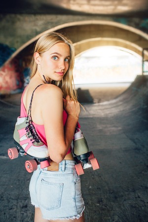 Vertical picture of beautiful and confident girl posing on camera. She is standing and looking back. Girl holds rollers hanging over her shoulder.の写真素材