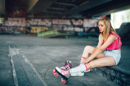 Serious girl is sitting and pulling back long laces on right roller. Girl is concentrated on this action. She is going to be ready for rollerblading.の写真素材