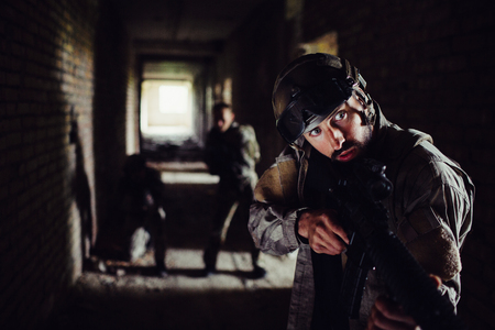 Three soldiers are standing in dark corridor and waiting. The guy in front is looking to the right and holding rifle in his hands. The other tow are standing on the back and covering him.の写真素材