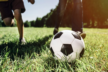 A picture of legs of two people playing football game. They are playing on green and juicy grass. It...