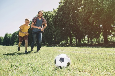 Father and son are playing football. They are running together. Boys want to reach the ball first.の写真素材