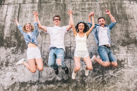 Awesome and nice people are jumping up in the air. They are holding their hands up in the air too. Company is on the grey background. They are positive and happy.の写真素材