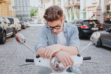 Handsome guy is sitting on motorcycle and looking down. He wears glassesの写真素材
