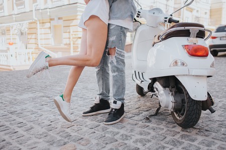 Girl is jumping near guy. Her legs are in air. They are standing beside motorcycle in the middle of street. They have a date today.の写真素材