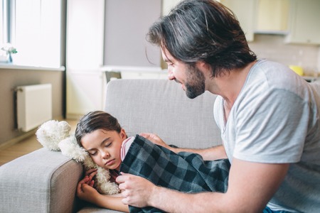 Careful parent is covering his daughter with blanket. She fell asleep. Guy looks at er and smiles.