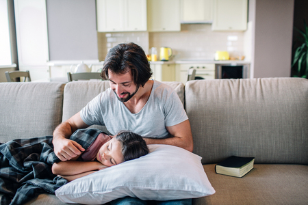 Nice picture of dad looking at daughter and smiling. She has fallen asleep. Girl is covered with blanket. Her head is lying on guys lap.の写真素材
