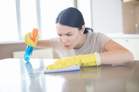 Careful and concentrated woman is spraying on surface of table and cleaning it with rag.の写真素材