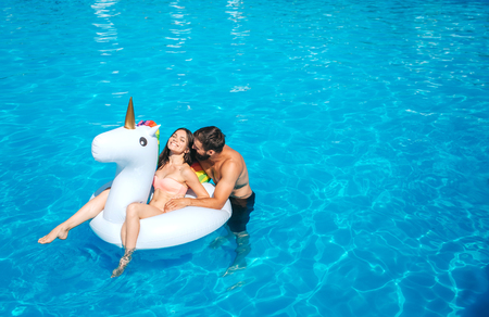 Nice and positive picture of man and woman swimming in pool. Girl sits on air mattress. She is laughing. Guy stands besides her and leans to her. They have some rest.の写真素材