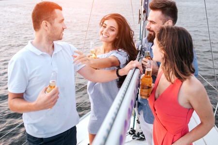Beautiful picture of brunette touches man and smiles. Another couple standing in front of them. They have bottles of beer. People relax and chill.の写真素材