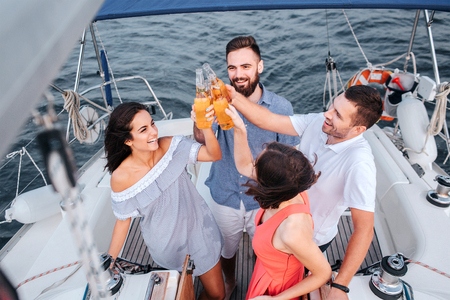 Four people standing close to each other and cheers with bottles of beer. They look up and smile. People are happy.の写真素材