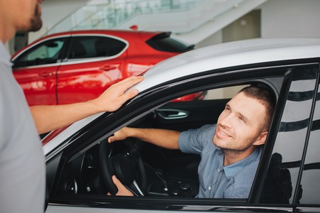 Handsome and satisfied young men sitting in white car and look at manager. He smiles. Guy hold hands...