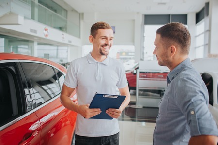 Picture of customer and seller stand together in front of beautiful red car.の写真素材