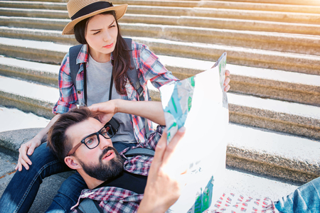 Picture of serious tourists on steps. He is lying on girlfriends knees and hold map in hanad. She sits on steps. They are confused and concentrated.の写真素材