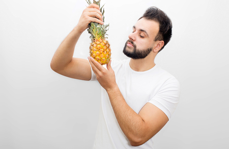Picture of man standing and holding pineapple. He looks at it with seriousness. Isolated on white background.の写真素材
