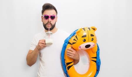 Picture of young bearded man standing and chilling. He drinks milk and hold kids baby float in hand....
