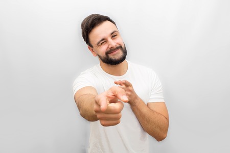 Very positive young man points on camera and whinkles to it. He smiles. Isolated on white background.の写真素材