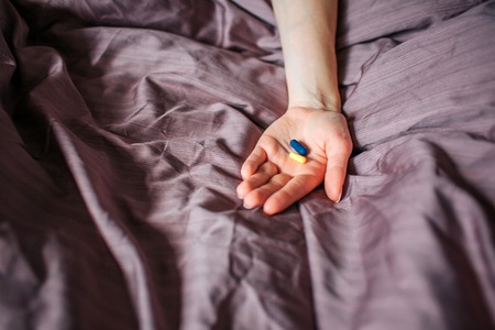 Picture of hand on violet blanket holding different kind of medicine on hand. There are two capsules: yellow and blue. Close up.の写真素材
