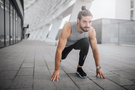 Picture of young man ready to run. He stands in sprint position and look straight forward. Guy is ready to run fast. He is strong and well-built.の写真素材