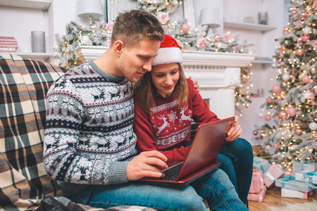 Concentrated and interested young man and woman works using laptop. They look at it. Guy pushes buttons. They wear festive clothes.の写真素材