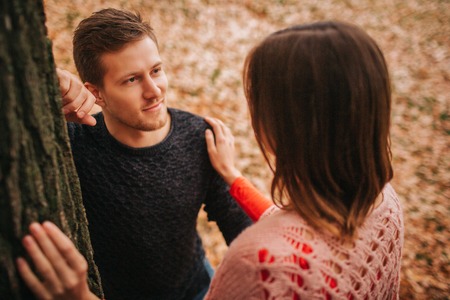Handsome young man look at woman and smile. He is in love. Woman touches him. He leans on wood.の写真素材