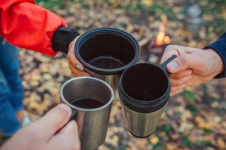 Picture of three thermocup that is hold by one woman and two mens hands. They do it together. People are in forest.の写真素材