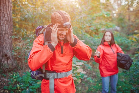 Picture of young man holding hands on head. He has headache. Young woman stands behind him and reaches with hand.の写真素材