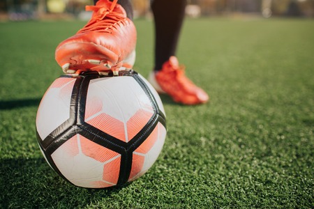 Pictre of mans leg on football ball. Another one stand on green lawn. It is sunny outside.の写真素材