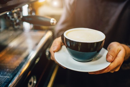 Close up of big cup of coffee. Mans hands hold it. Guy stand at coffee machine.の写真素材
