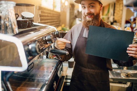 Excited young man points on piece of dark paper. He hold it in hand and look on camera. Guy stand at...