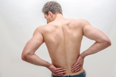 Young man stand and hold hands on back. He feels pain in kidneys area. Isolated on white background.
