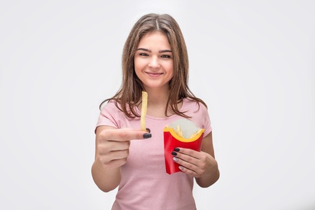 Happy young woman hold piece of fried potato and look at it. She is happy. Another pieces of...