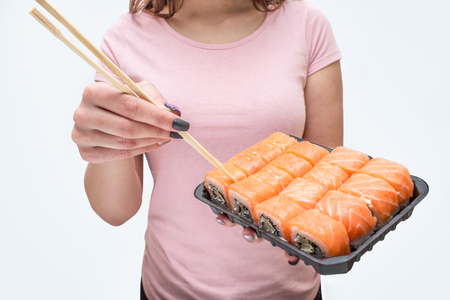 Cut view of young woman hold plate with sushi. She touch them with chopsticks. Isolated on white background.の写真素材