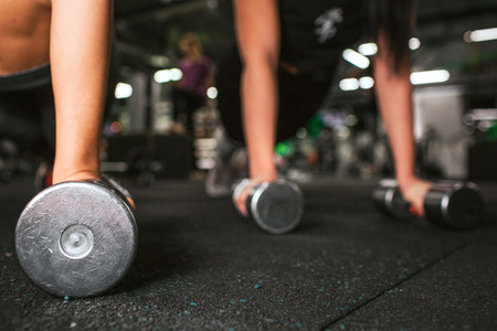 Cut view of two pair young women's hands standing on dumbbells. They work together on same floor in gymの写真素材